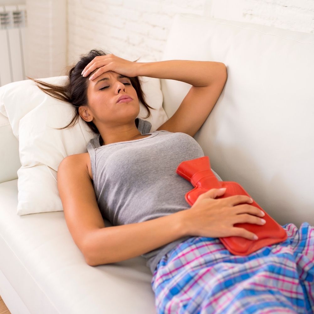 Une belle femme brune allongée sur un canape, une bouillotte sur le ventre pour calmer les douleurs liées aux règles
