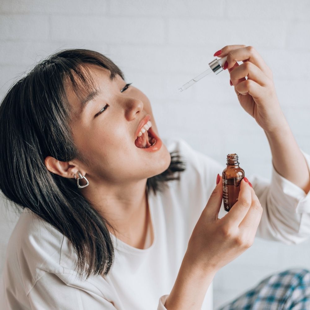 Une femme brune aux cheveux courts prends quelques gouttes d'huile de cbd règles douloureuses délicure sous la langue