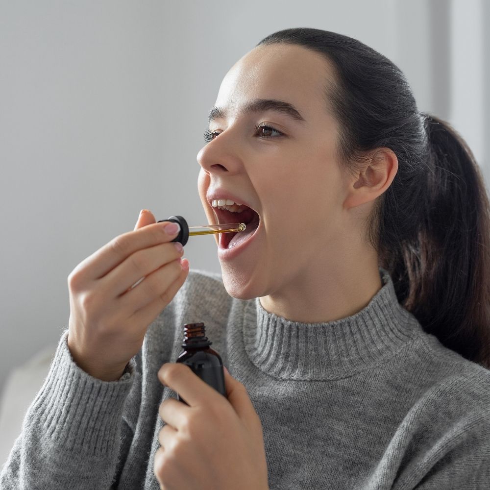Une jeune femme brune met des gouttes d'huile de cbd sous la langue en souriant