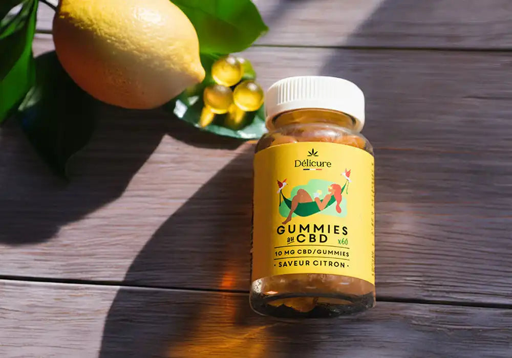pot de gummies cbd délicure posé sur une table en bois, vu de dessus avec un citron et quelques gummies au cbd dispersés sur la table