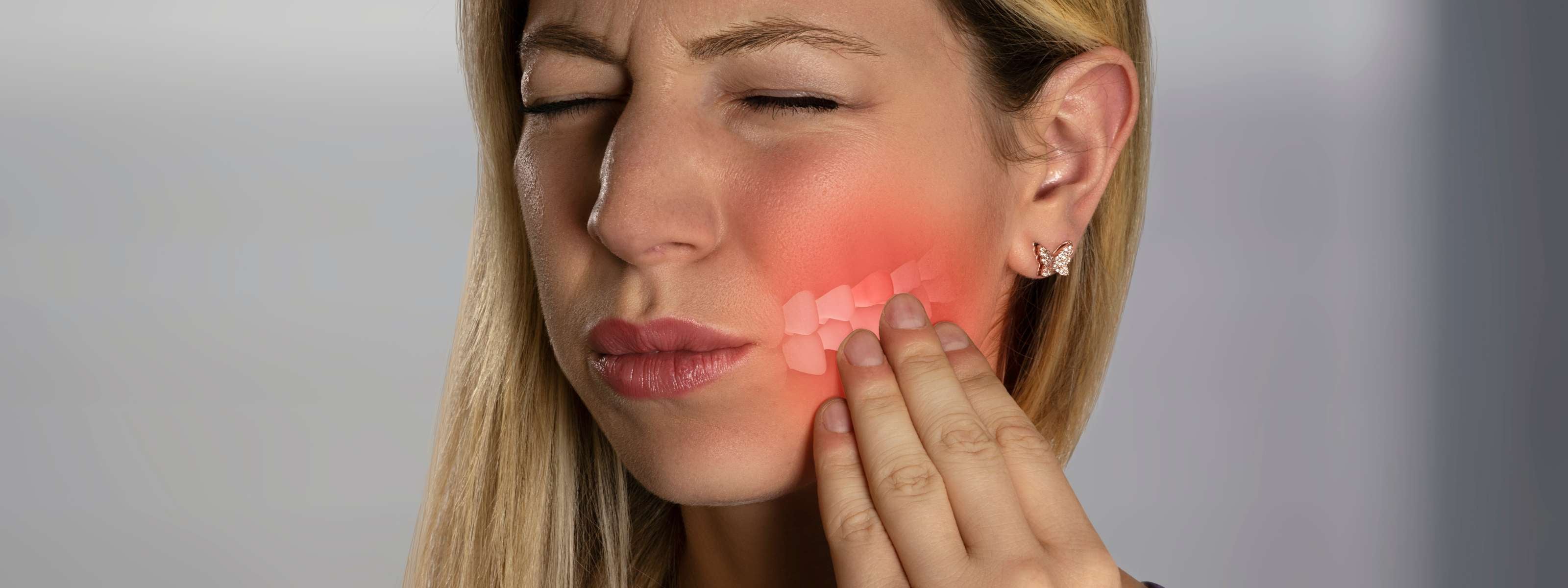 Femme grimaçant et tenant sa joue, douleur dentaire localisée.