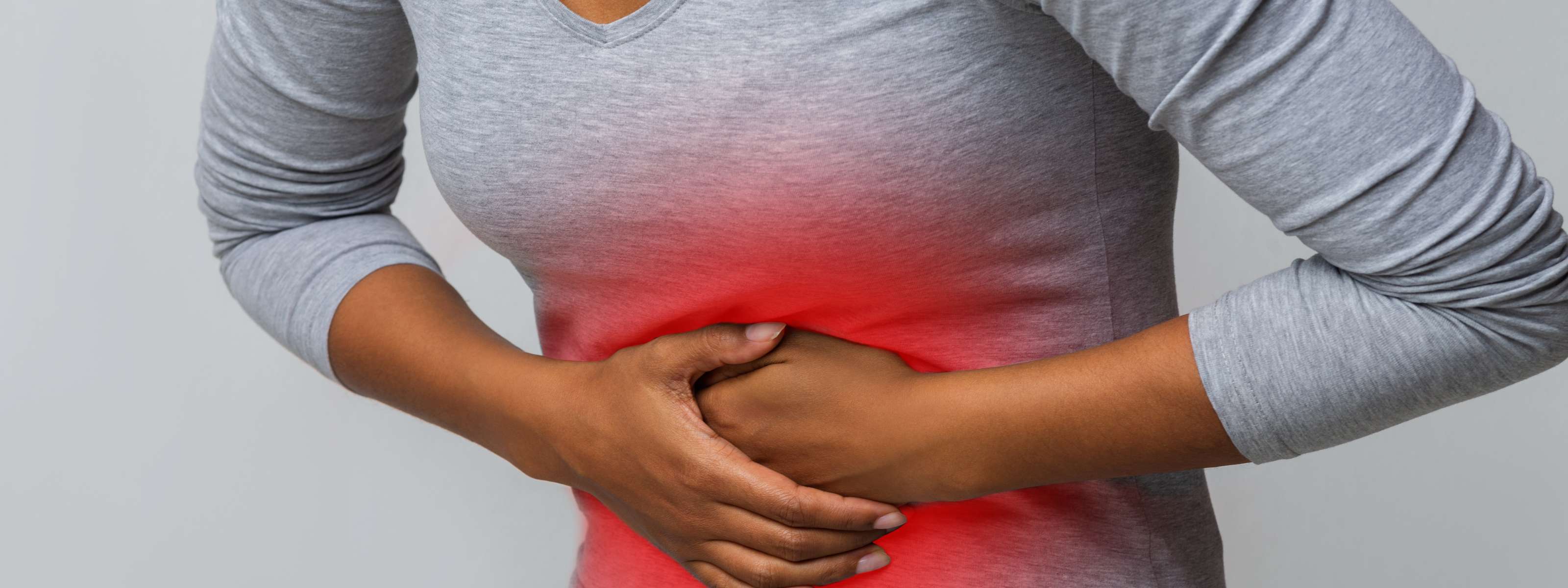 Femme posant ses mains sur le ventre, avec une douleur abdominale visible.