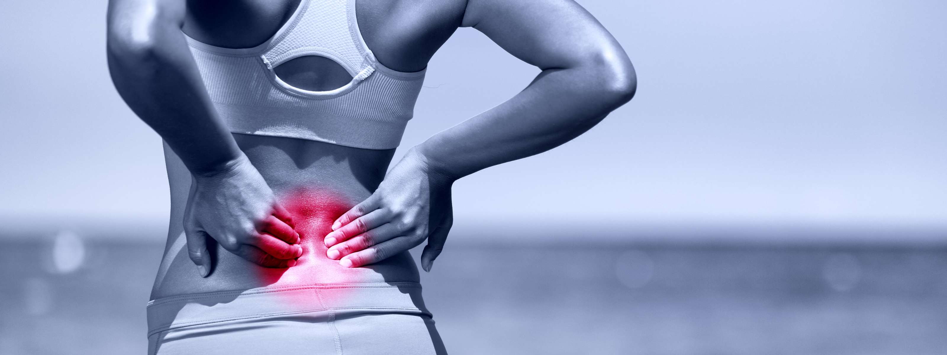 Femme de dos touchant ses lombaires, douleur au bas du dos.