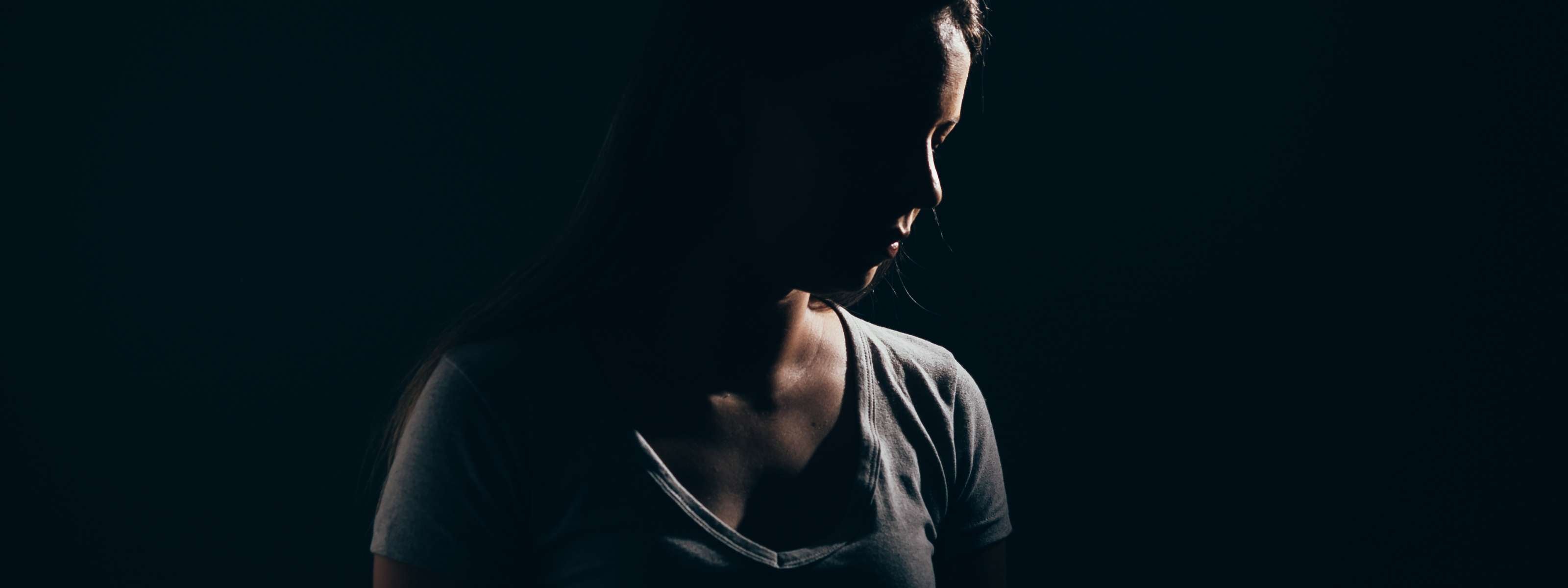 Femme seule dans l’ombre, posture triste ou anxieuse.