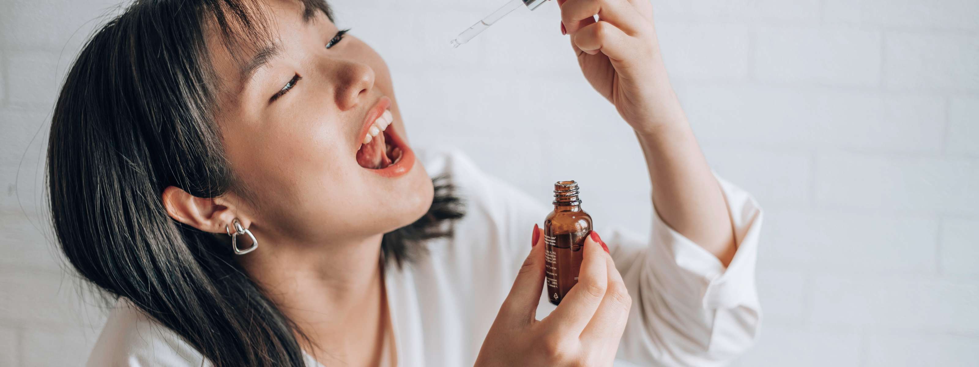 Femme souriante prenant de l’huile de CBD avec une pipette.