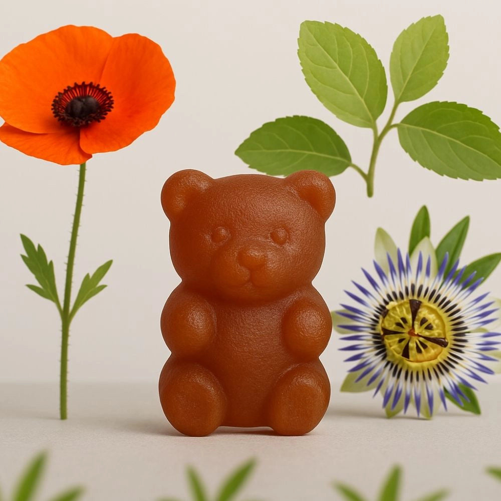 Gummy en forme d’ourson posé devant une fleur de coquelicot et une passiflore, représentant la synergie de plantes dans la formule Sommeil radieux.
