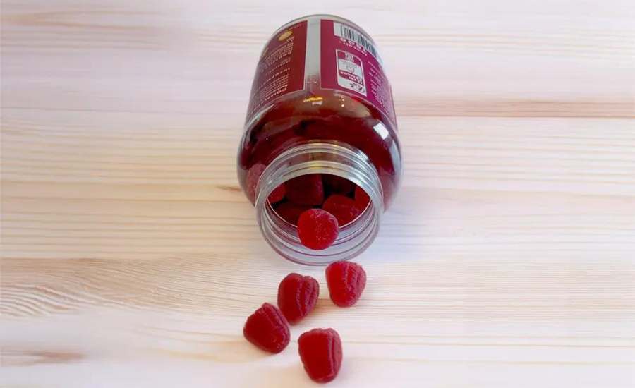 Un pot de gummies au cannabidiol arôme framboise couché sur une table en bois clair, le pot est ouvert et laisse échapper quelques gummies au cbd.