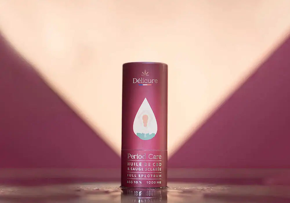 Image d'un flacon de complément alimentaire Délicure Period Care contenant de l'huile de CBD et de la sauge sclarée, en version Full Spectrum et dosé à 1000 mg. Ce produit est conçu pour le soin et le confort pendant les périodes menstruelles. La photo est prise sur un fond aux tons pourpres et beiges, créant une ambiance apaisante et élégante.