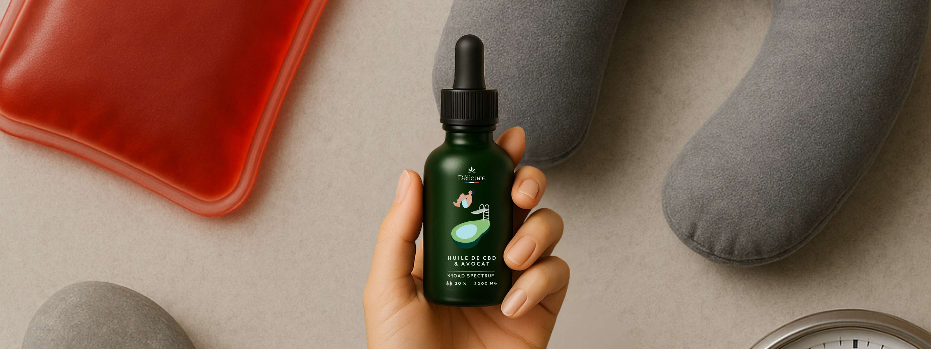 Main tenant un flacon d’huile de CBD Délicure posée sur une surface avec galets et horloge, illustrant un rituel naturel contre les maux de tête.