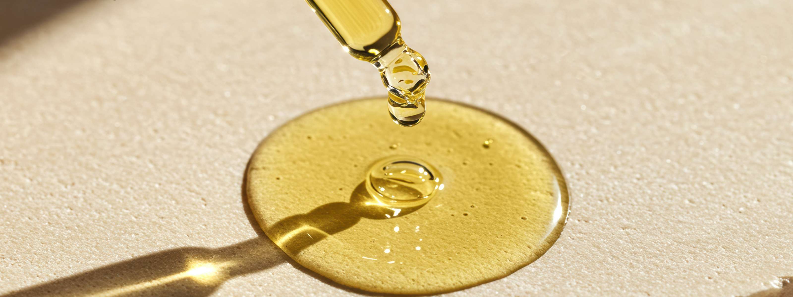 Goutte d’huile de CBD tombant d’une pipette sur une surface dorée.