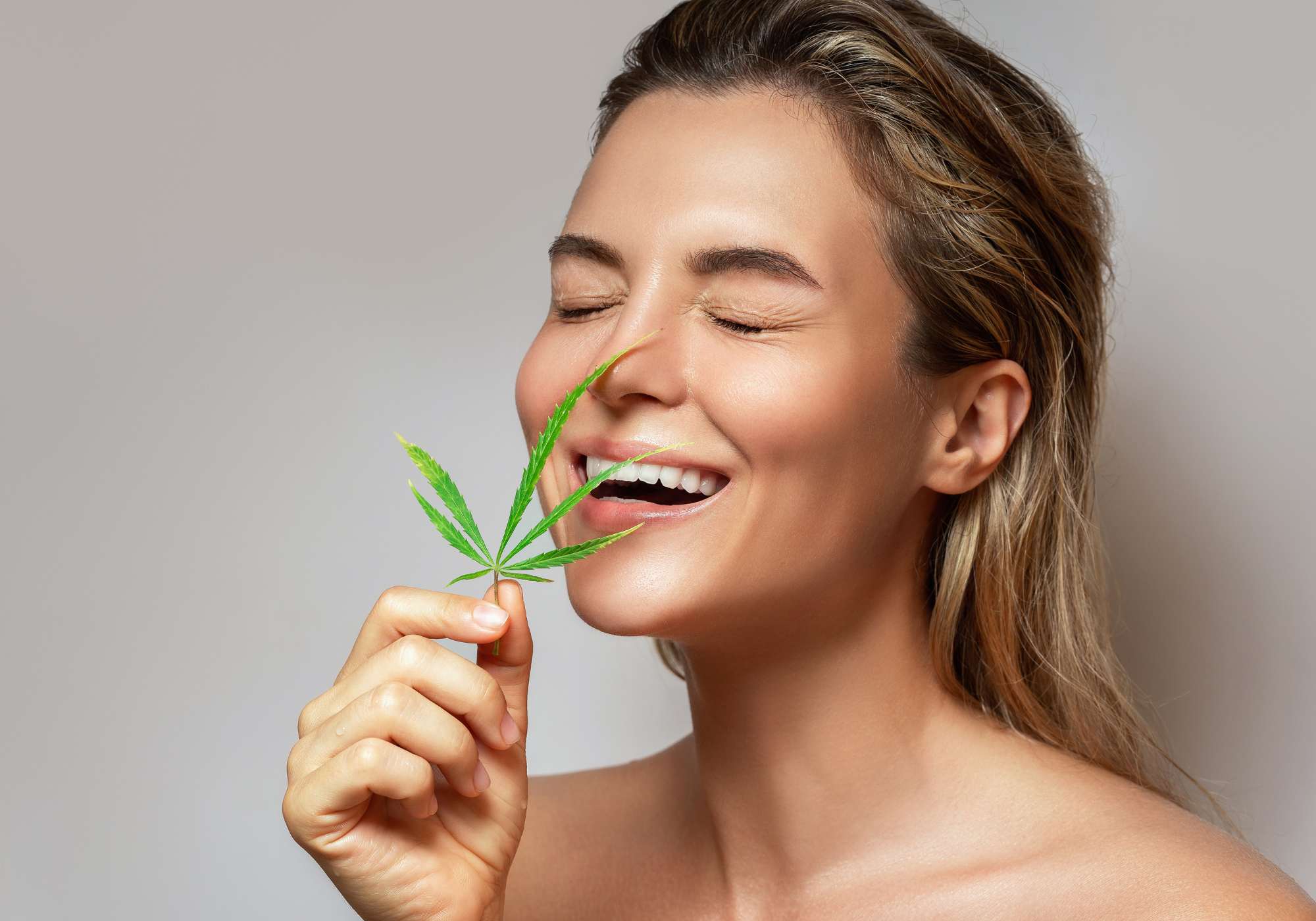 Femme détendue tenant une feuille de chanvre près de son visage, symbolisant les bienfaits relaxants du CBD sur le sommeil.