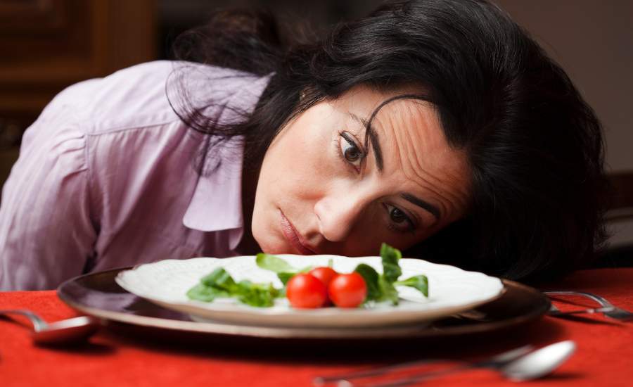 femme regardant une assiette presque vide Exemple de régime trop restrictif pouvant ralentir le métabolisme et provoquer une baisse d’énergie