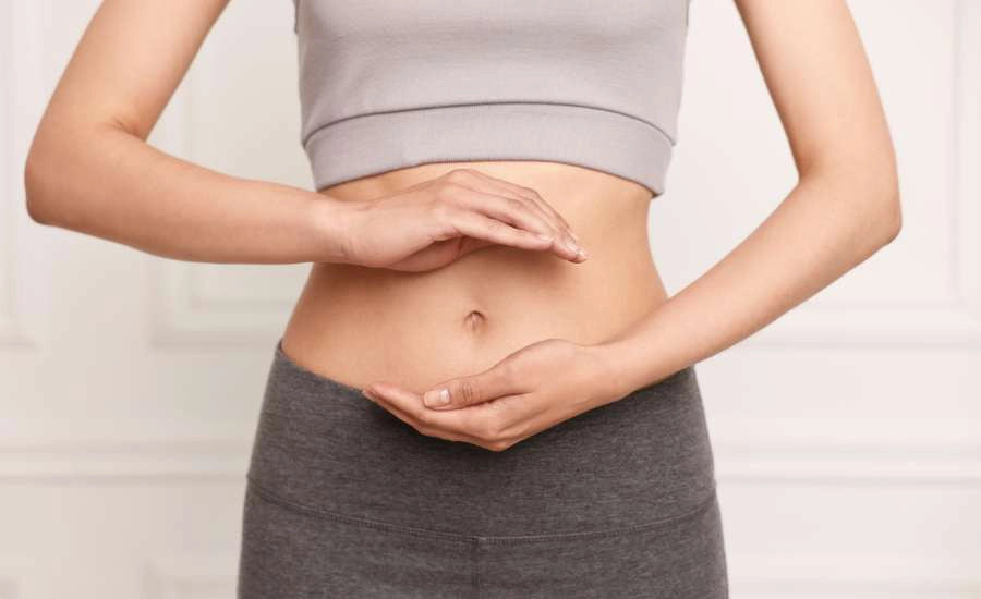 Primo piano del busto di una donna in abbigliamento sportivo grigio, con le mani che formano un cerchio attorno all'addome, a dimostrazione del benessere intestinale favorito dalla curcuma.